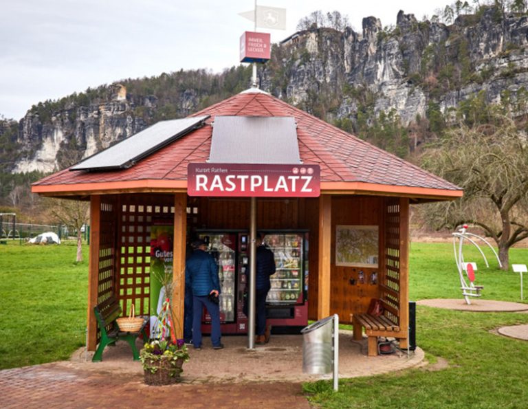 Unter einem Pavillon mit der Aufschrift „Rastplatz“ stehen zwei Verkaufsautomaten.