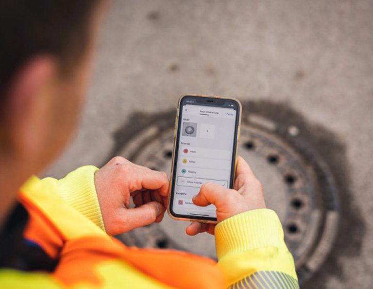 Eine Person hält ein Smartphone über einen Gulli.