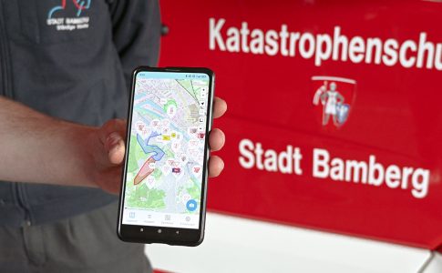 Ein Smartphone, das einen Stadtplan zeigt, vor einem Einsatzfahrzeug.