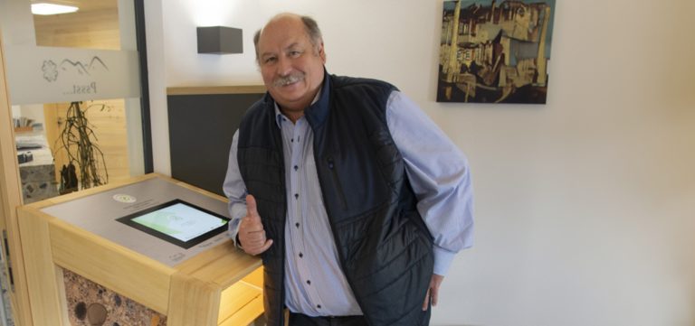 Mann, der vor einem Anmeldeterminal mit Tablet steht.