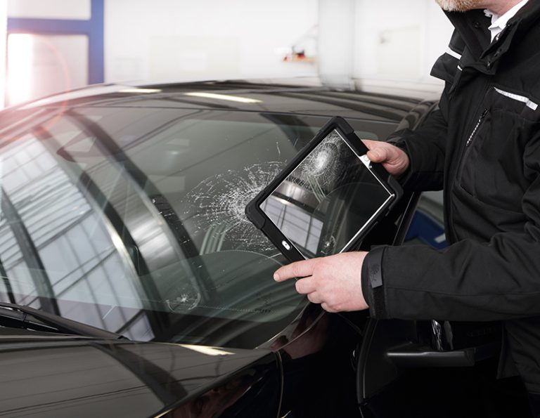 Person mit Tablet-Computer dokumentiert den Schaden in einer Windschutzscheibe.