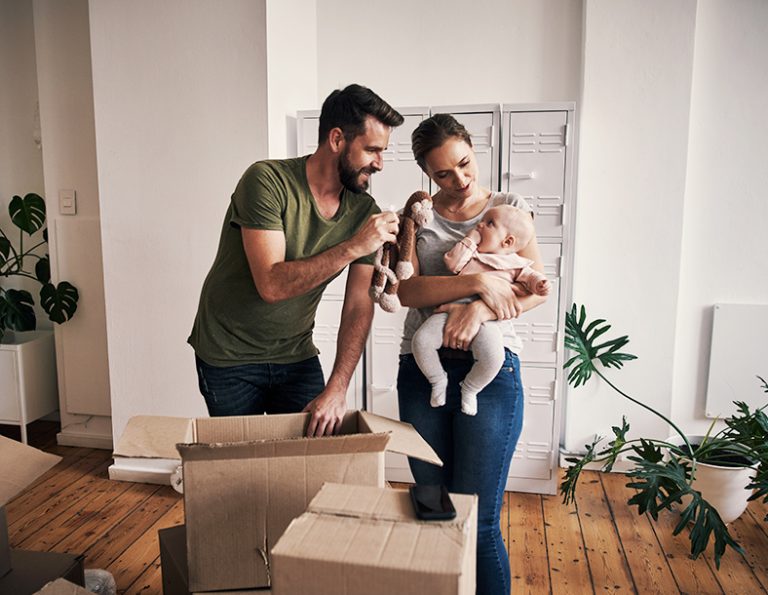 Frau, Mann und Baby stehen in einem Zimmer vor Umzugskartons.