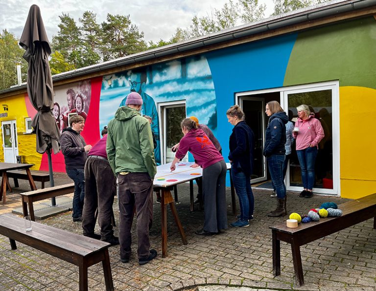 Menschen um einen Tisch herum vor einem bunten Gebäude im Freien.