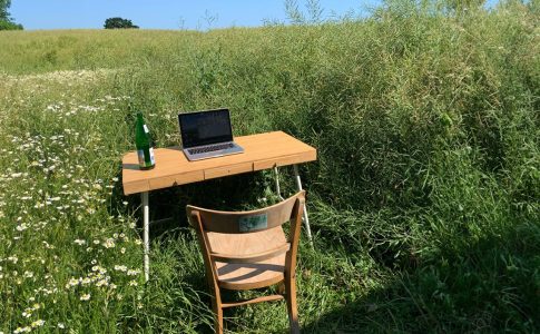 Ein Schreibtisch mit Stuhl und Laptop auf einer grünen Wiese