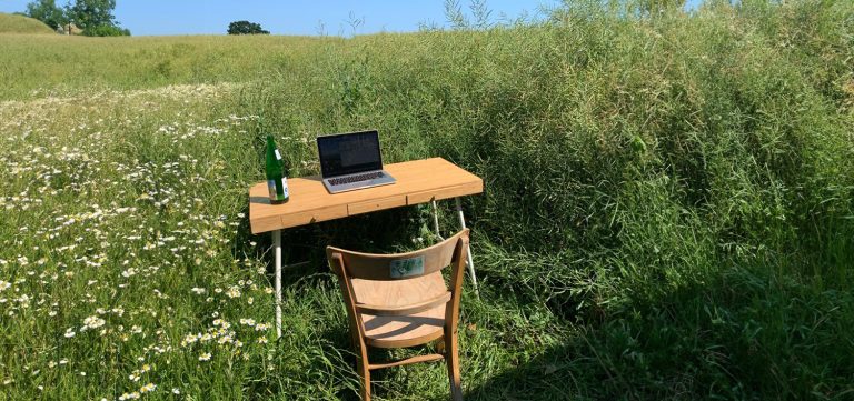 Ein Tisch mit Laptop und ein Stuhl stehen auf einer grünen Wiese.