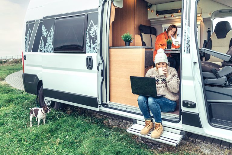Zwei Frauen sitzen in einem Campingbus und arbeiten am Laptop.