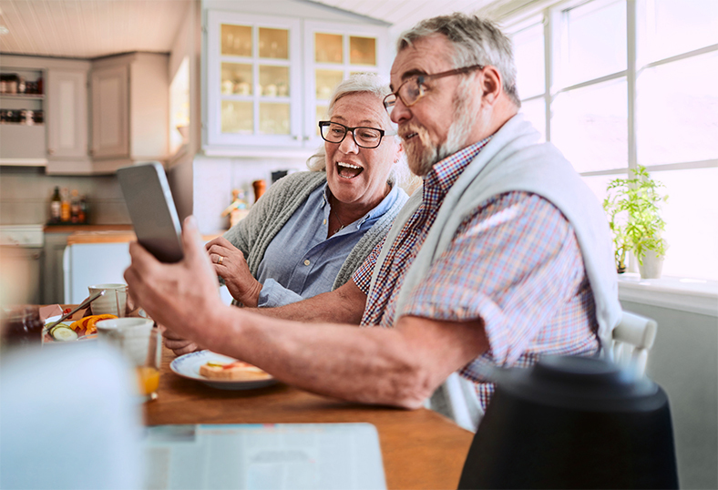 Ältere Frau und älterer Herr mit Tablet am Frühstückstisch