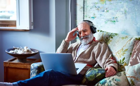 Älterer Herr mit Laptop und Kopfhörern auf geblümten Sofa