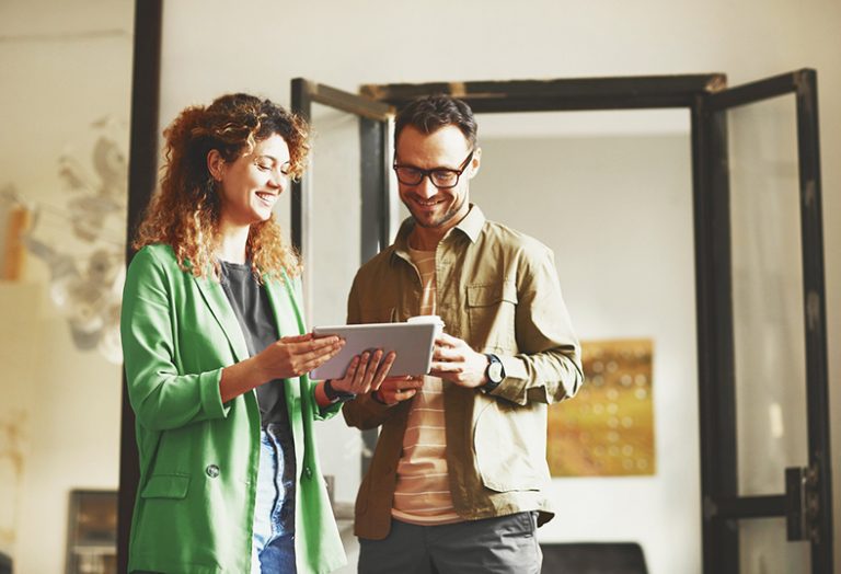 Frau und Mann stehen in einer Wohnung vor einer offenen Tür und schauen gemeinsam auf einen Tablet-Computer.