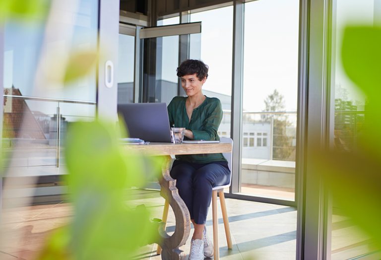 Eine Frau sitzt an einem Tisch und arbeitet an einem Laptop.