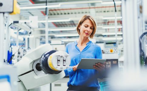 Eine Frau mit blauem Hemd steht vor einem technischen Gerät in einer Laborumgebung.