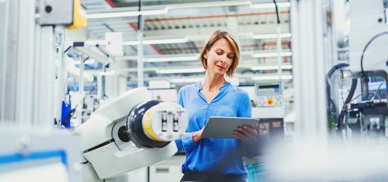 Eine Frau mit blauem Hemd steht vor einem technischen Gerät in einer Laborumgebung.